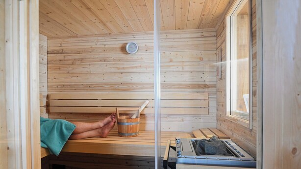 A sauna room with wooden walls, a bench, a bucket, and a sauna heater. - Romantic mill arbor "At the foot of the Staffelberg" (Bad Staffelstein)
