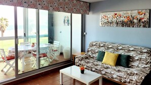 Uma sala de estar com um sofá, uma mesa de centro e uma porta de vidro que dá para uma varanda.