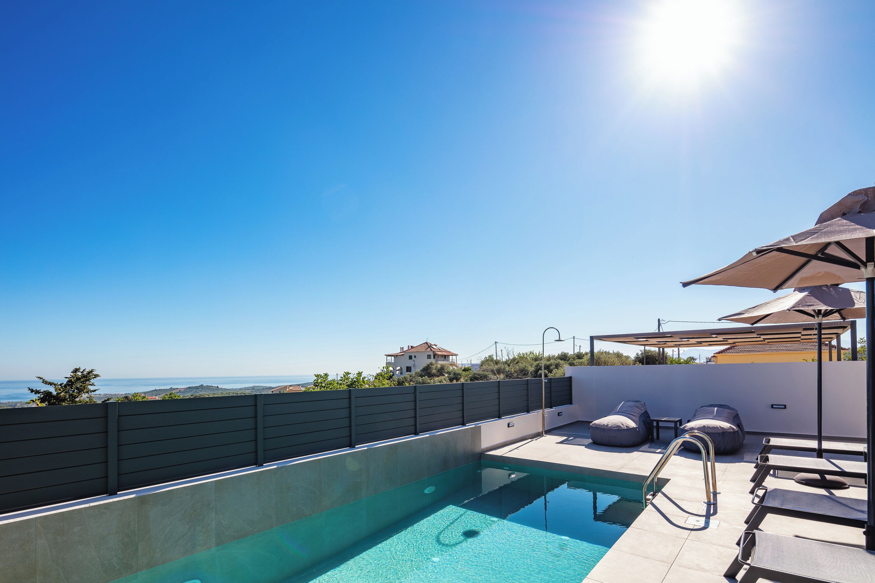 A rooftop pool with clear blue water, a view of the sea, and outdoor seating with umbrellas.