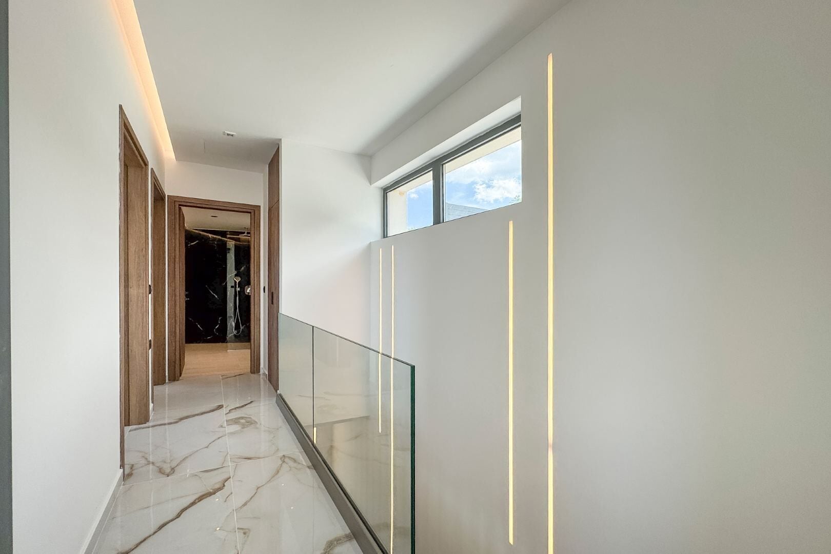 A modern hallway with marble flooring, glass railings, and recessed lighting.