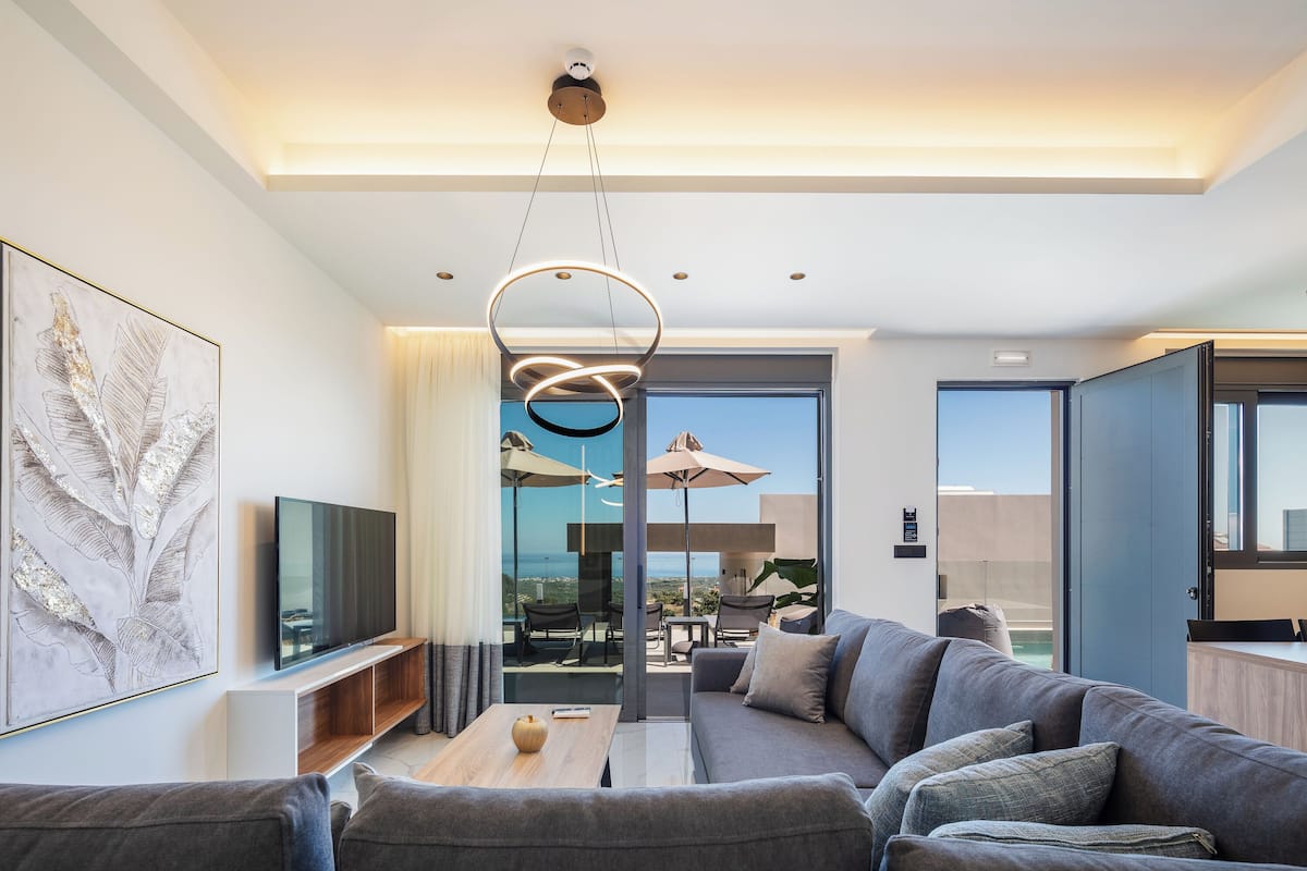 Ein modernes Wohnzimmer mit grauem Sofa, einem Flachbildfernseher und einer Deckenleuchte.