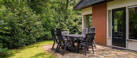 A patio with a table and chairs, surrounded by lush greenery and a brick wall.