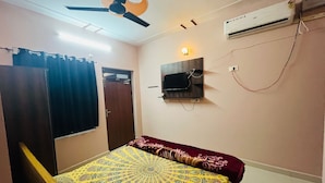 A bedroom with a bed, a ceiling fan, an air conditioner, a TV mounted on the wall, and a door. - Shree Raj Homestay (Faizabad)