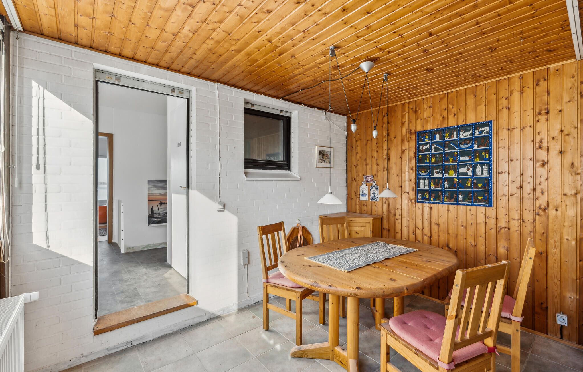 A wooden-paneled room with a round wooden table and chairs, a white brick wall, and a wooden ceiling.