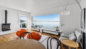 A modern living room with a large window, a fireplace, orange chairs, a grey sofa, and a wooden table. - Nice home in Wunstorf/Steinhuder (Wunstorf/Steinhuder)