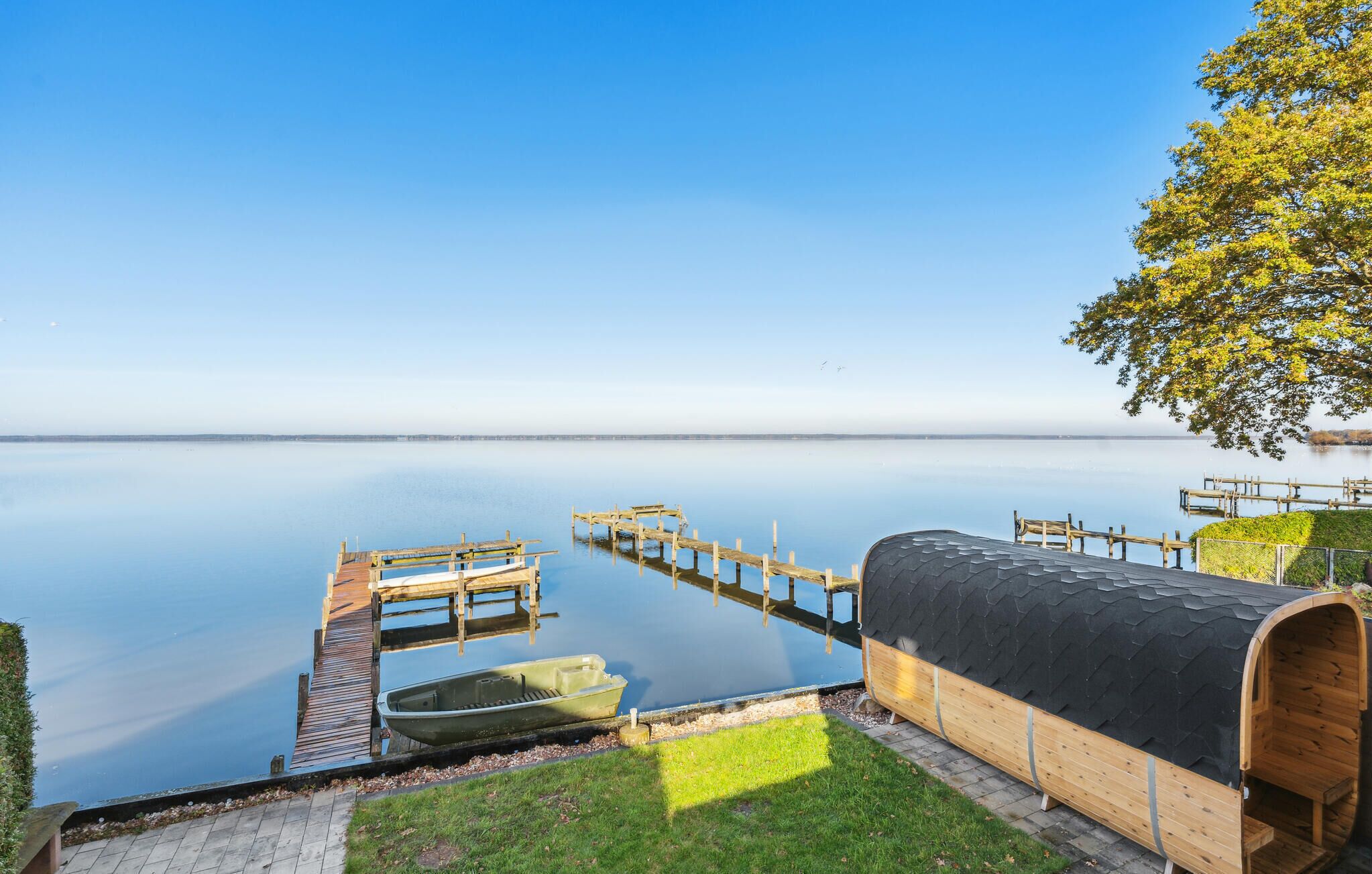 Una escena tranquila junto al lago con un muelle de madera, una estructura cubierta de madera y una vista despejada del lago.