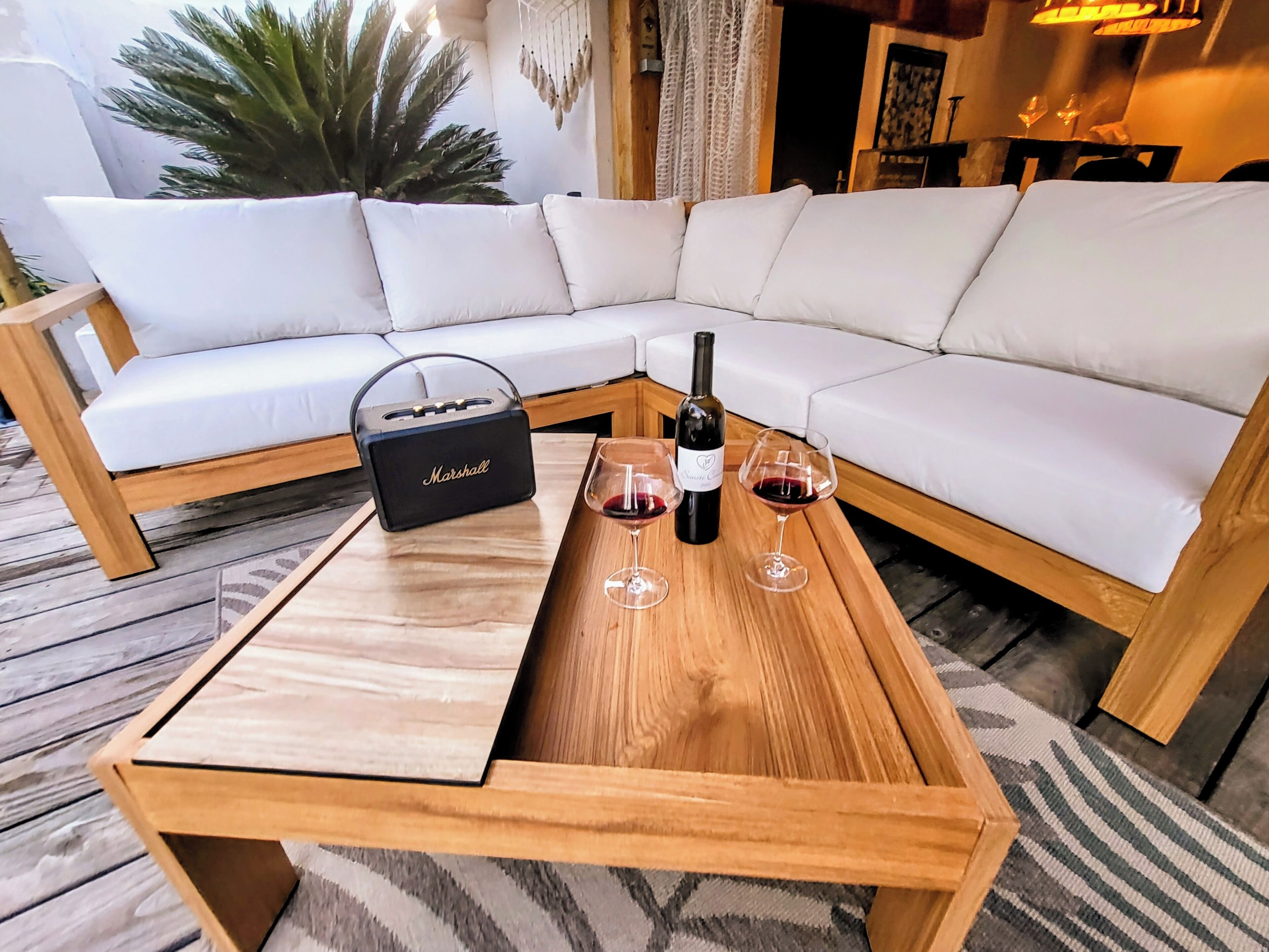 Een houten bijzettafel met een witte kussen, een Marshall speaker, een fles wijn en twee wijnglazen.