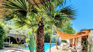 A wooden deck with a pool, a palm tree, and outdoor furniture. - HOUSE "L'OLIVETTE" jacuzzi, heated pool, billiards, table soccer, 7KM from Nîmes  (LANGLADE)