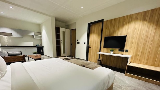 A modern hotel room with a large bed, a flat-screen TV mounted on a wooden wall, and a small bedside table.