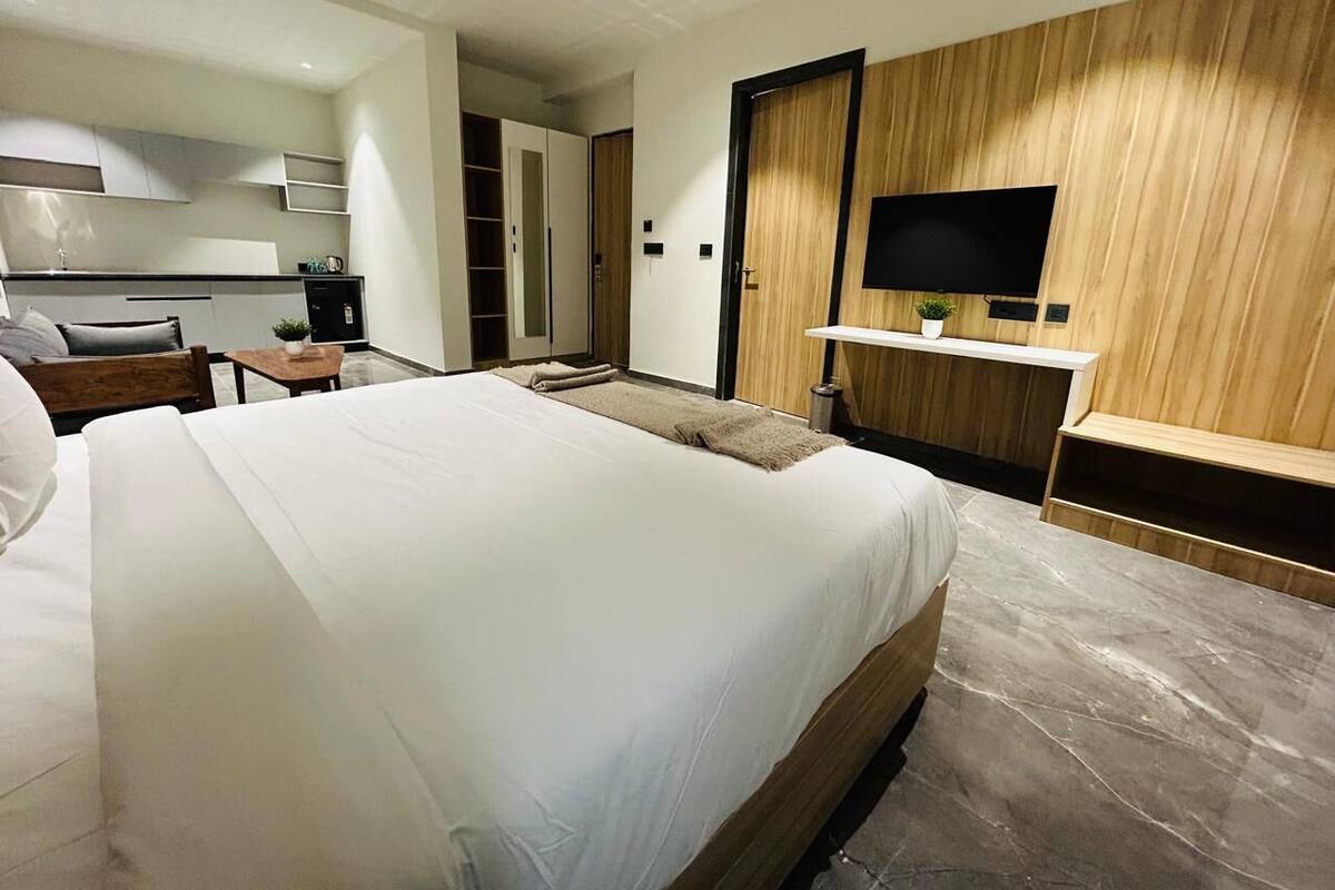 A modern hotel room with a large bed, a flat-screen TV mounted on a wooden wall, and a small bedside table.