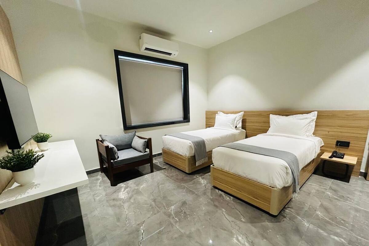 A modern hotel room with two beds, a desk, and a chair.