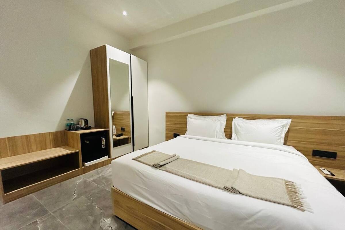 A modern hotel room with a large bed, a wooden wardrobe, a small desk, and a mirror.