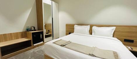 A modern hotel room with a large bed, a wooden wardrobe, a small desk, and a mirror.
