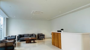 A modern reception area with a white reception desk, a wooden accent wall, and a seating area with sofas and chairs.