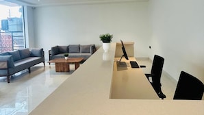 A modern office space with a long reception desk, two sofas, a coffee table, and a potted plant.