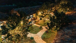 Estructura con techo de paja y un sendero de piedra que lleva a una zona de estar, rodeada de abundante vegetación y luces colgantes.