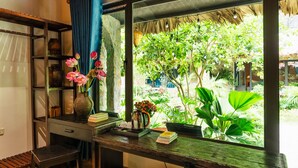 Una habitación con un ventanal grande, un escritorio de madera, una silla, una estantería y una planta en maceta.