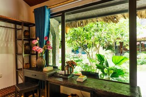 A room with a large window, a wooden desk, a chair, a bookshelf, and a potted plant.