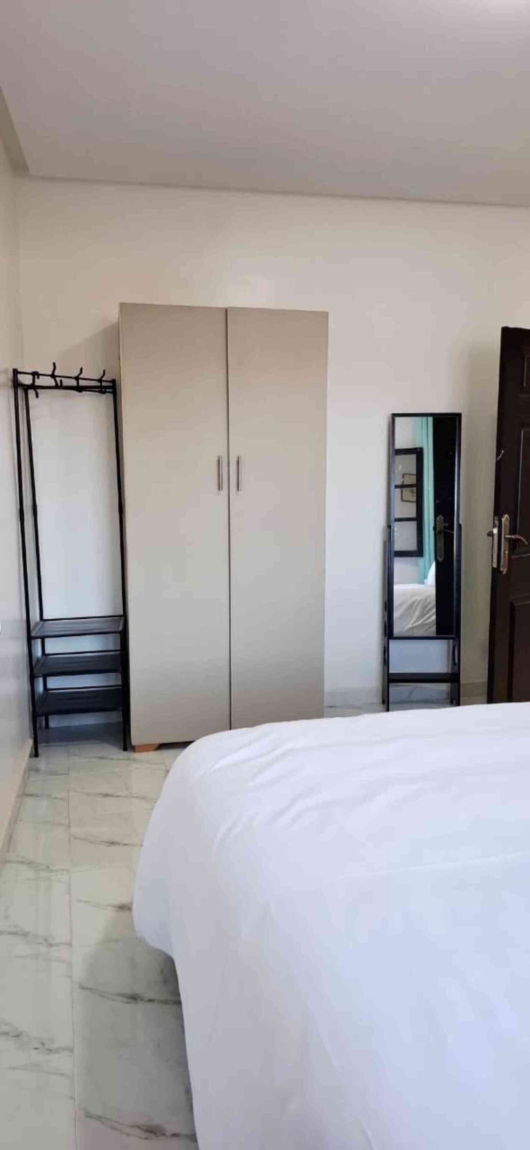 Een hotelkamer met een bed, een kledingkast, een spiegel en een kapstok.