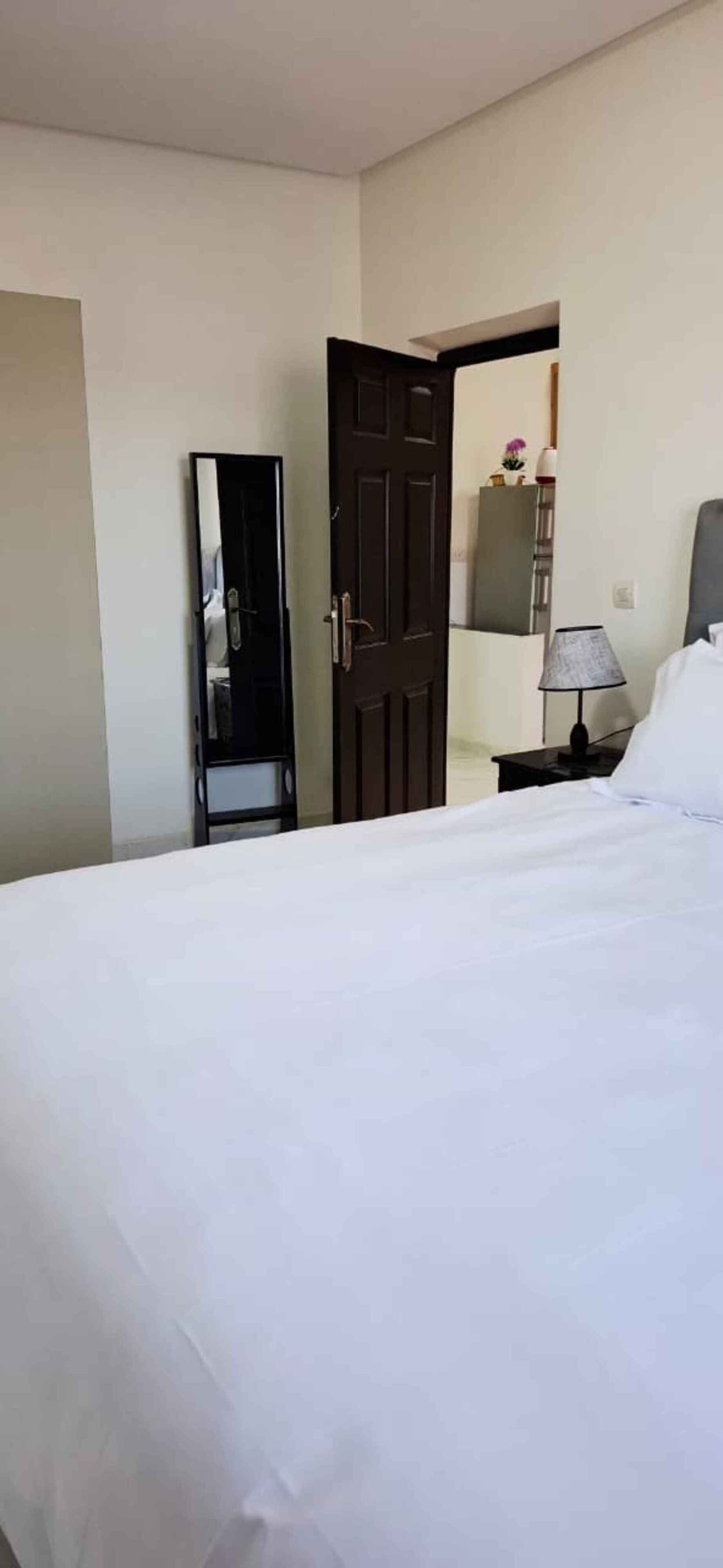 A hotel room with a bed, a nightstand, a lamp, a mirror, and a wardrobe.