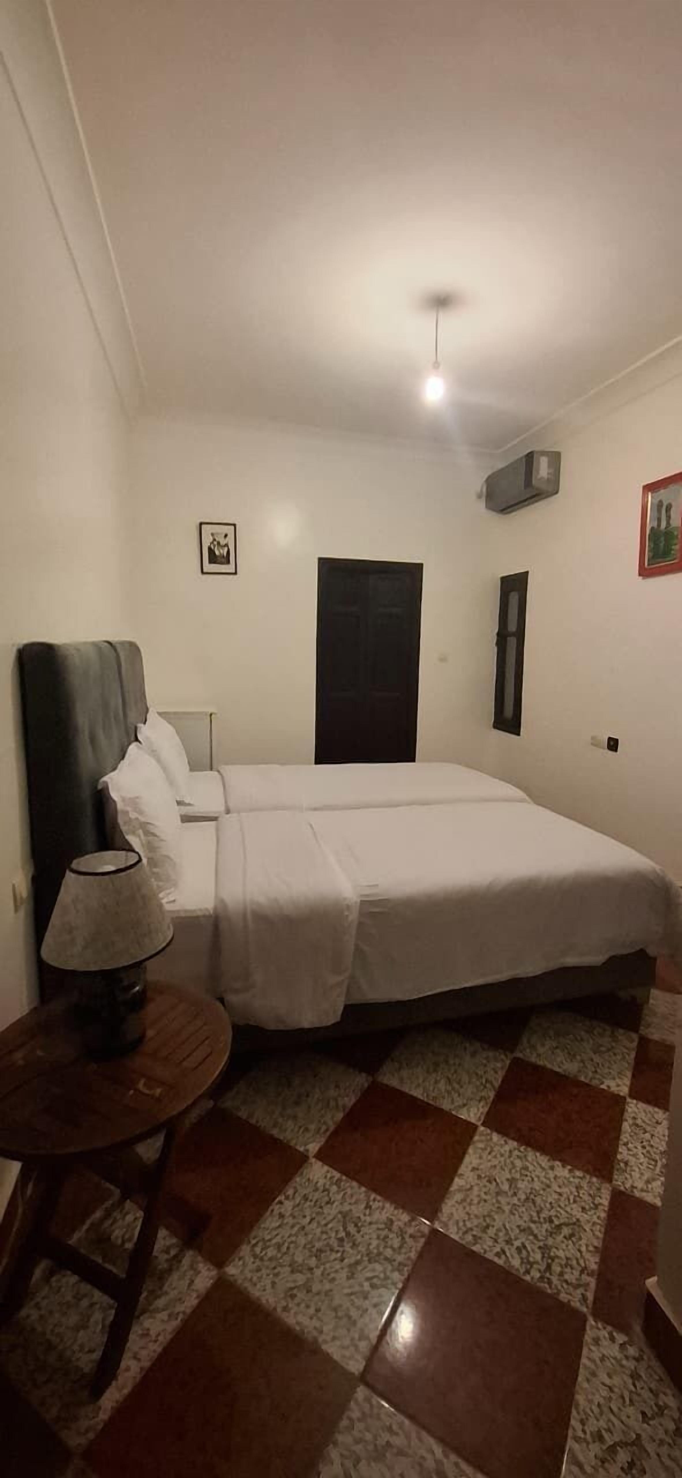Un dormitorio con cama, mesita de noche, lámpara, puerta y piso a cuadros.