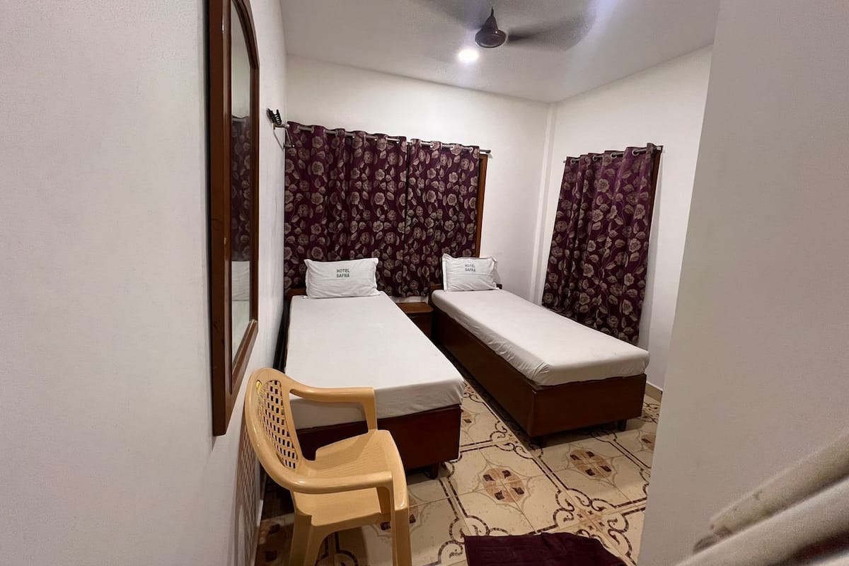 A small, clean room with two single beds, a wooden chair, and a ceiling fan.