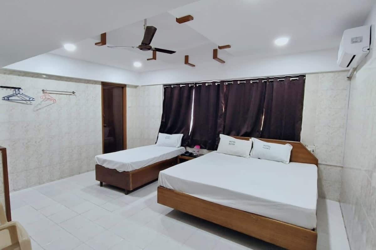 A hotel room with two single beds, a desk, a chair, a ceiling fan, and a window with curtains.