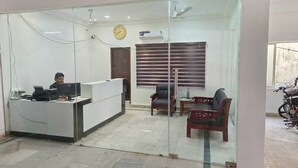 An office with a reception desk, two chairs, a clock, and a window with blinds. - hotel safra (Chennai)