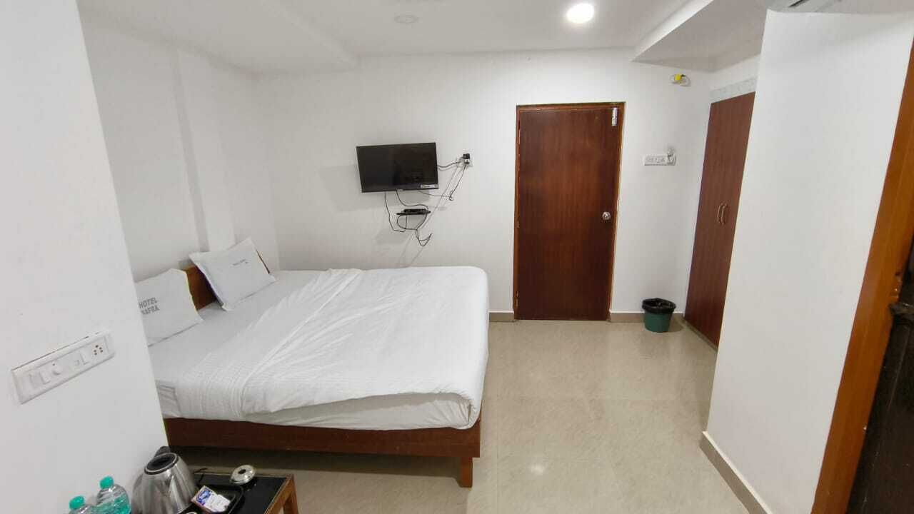 Un dormitorio con una cama, un televisor montado en la pared, una puerta de madera y un pequeño cubo de basura.