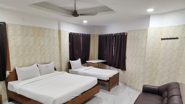 A hotel room with two beds, a small table, a sofa, and a ceiling fan. - hotel safra (Chennai)