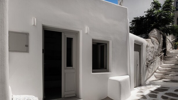 Un edificio blanco con una escalera que lleva a una puerta, un ventanal pequeño y un accesorio de iluminación en la pared.
