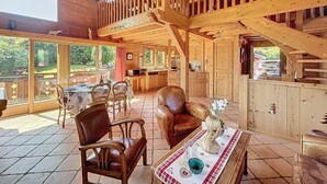 A spacious wooden cabin with a dining area, a kitchen, and a balcony with a view of the surrounding landscape.