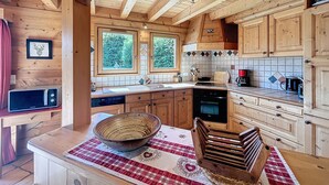 A wooden cabin interior with a kitchen area featuring wooden cabinets, a stove, and a large window.