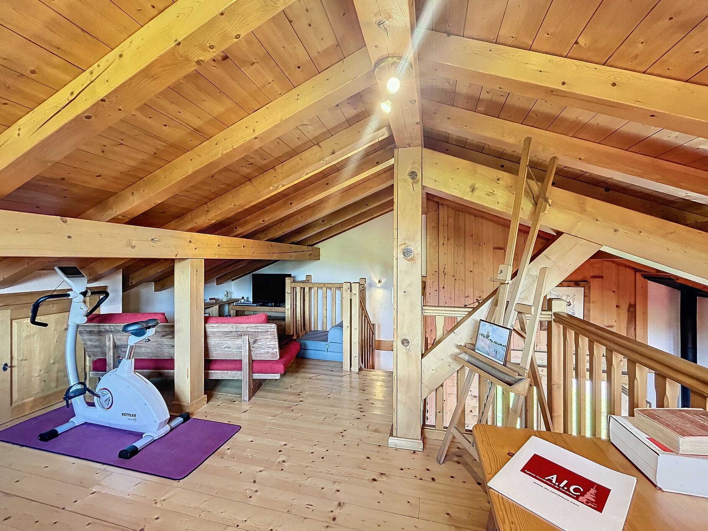 A wooden interior with a ceiling fan, exercise equipment, a staircase, and a book on a table.