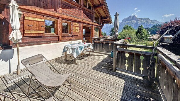 A wooden chalet with a balcony, outdoor seating, and a mountain view.