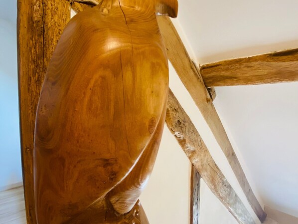 A wooden sculpture with a smooth finish, positioned against a white wall with visible wooden beams.