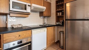 Een keuken met houten kastjes, een roestvrijstalen koelkast, een magnetron, een vaatwasser en een prullenbak.
