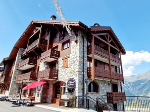 Een traditioneel chalet met stenen muren en houten balkons, met buiten zitplaatsen en een bord dat een restaurant aangeeft.