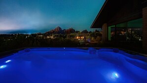 Un bain à remous avec vue sur le ciel nocturne, une chaîne de montagnes et un bâtiment illuminé.
