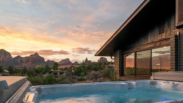 Un bain à remous avec vue sur les montagnes, un bâtiment en bois doté de grandes fenêtres et un ciel d égagé.