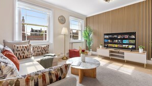 A modern living room with a large TV, comfortable seating, and large windows. - Stunning 2B Flat in South Kensington Near Station (London)