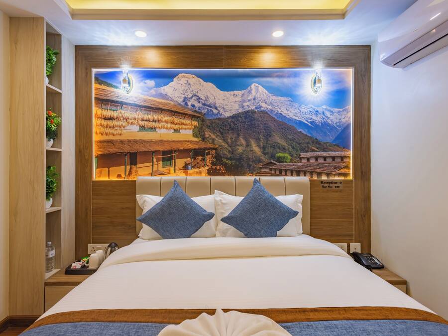 A hotel room with a large bed, a wooden headboard, and a mountain landscape mural on the wall.