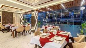 Un restaurante con mesas dispuestas para comer, vistas de la ciudad a través de amplios ventanales y un diseño interior moderno.