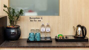 Zona de recepción con un cartel que indica “Recepción-0 Bar No-222”. Hay dos tazas azules, dos botellas de agua, una planta pequeña en una maceta negra y una tetera sobre una bandeja.