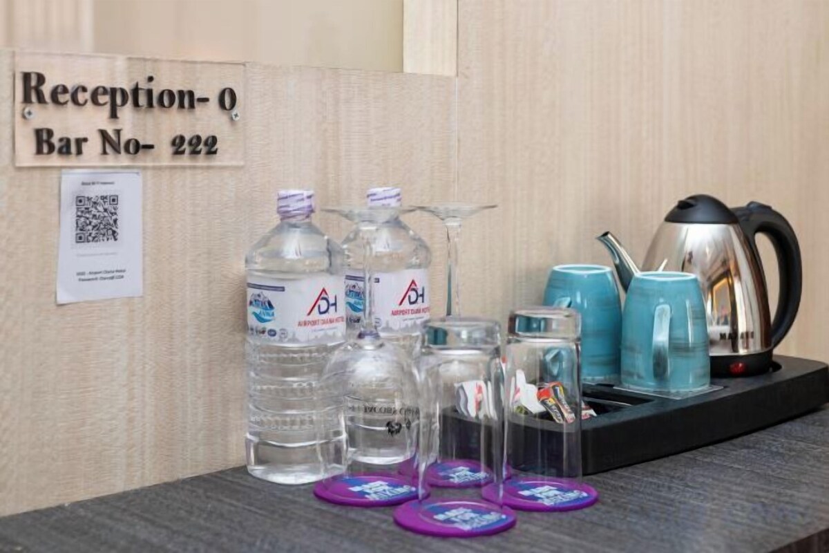 Zona de recepción con un cartel que indica 'Reception-0 Bar No-222'. Hay botellas de agua, un vaso, una tetera y una bandeja con tazas sobre la mesa.