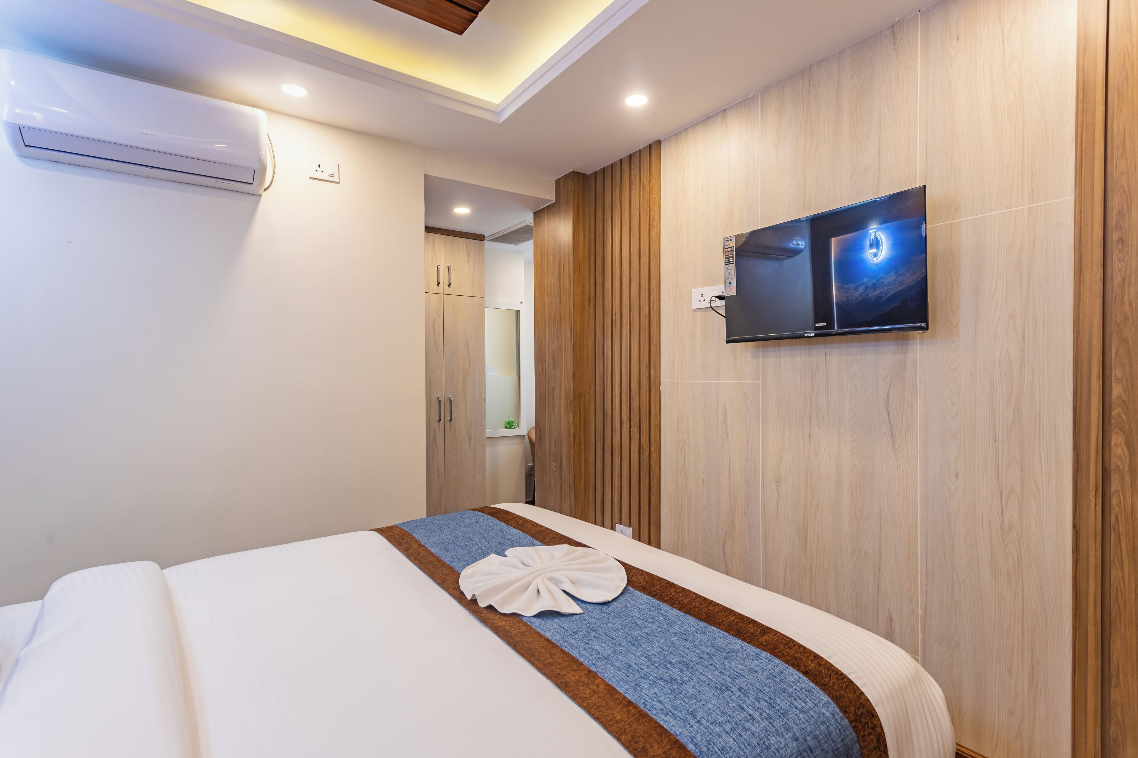 Ein Hotelzimmer mit einem Bett, einem an der Wand montierten Flachbildfernseher und einer Klimaanlage an der Wand.