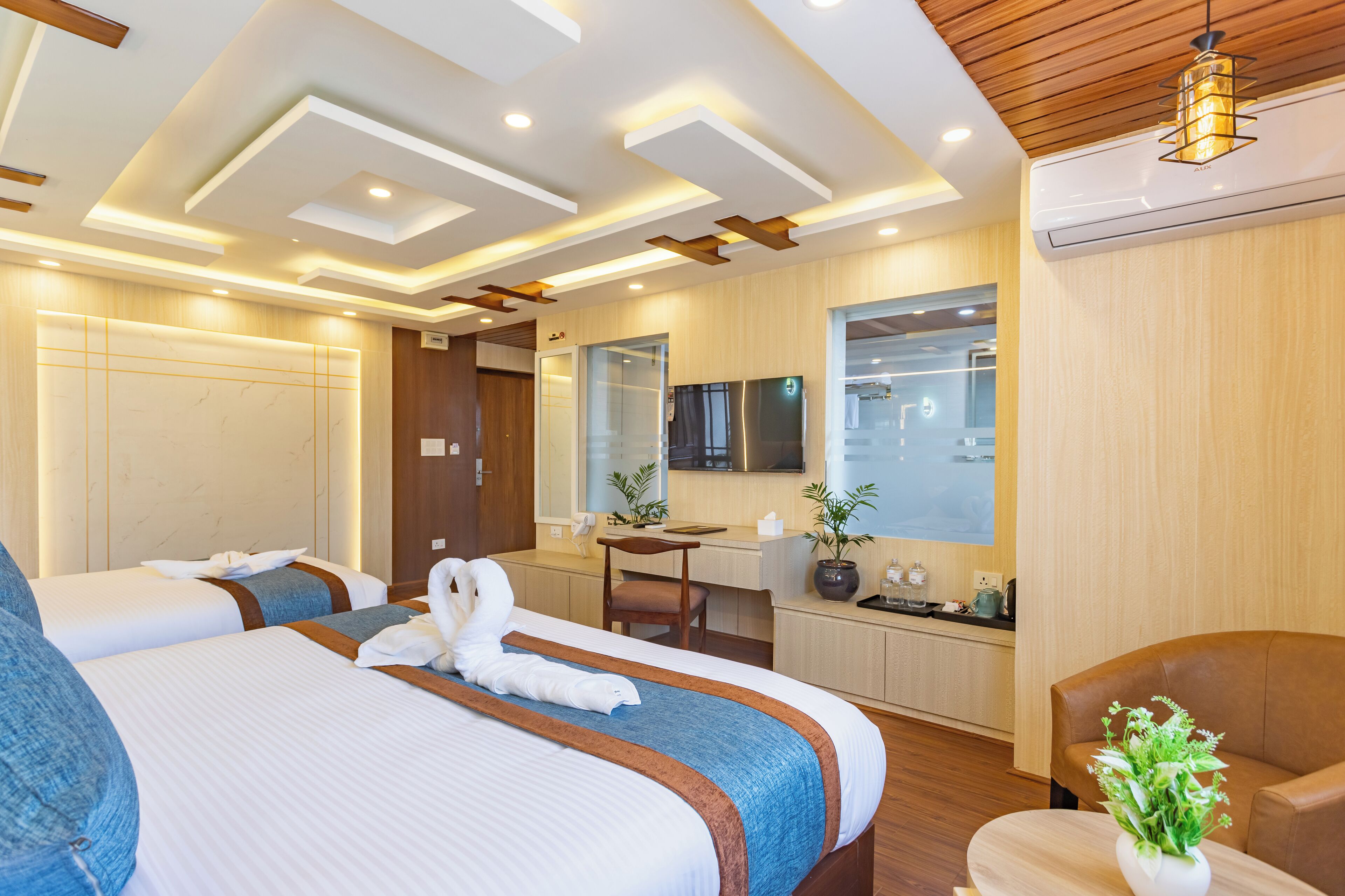 A modern hotel room with two beds, a desk, a chair, a TV, and a potted plant.