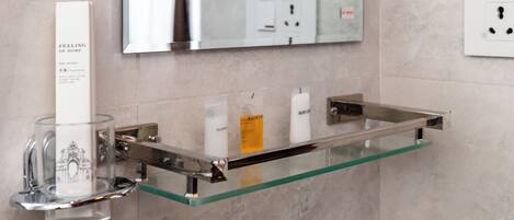 A bathroom with a glass shelf holding toiletries, a mirror above, and a wall socket.