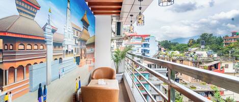 Un balcón con vistas a un paisaje urbano, una pintura de edificios y una mesa con sillas.