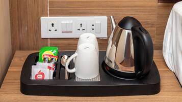A coffee maker, a kettle, and a tray with a bag of coffee and a packet of tissues on a black tray.